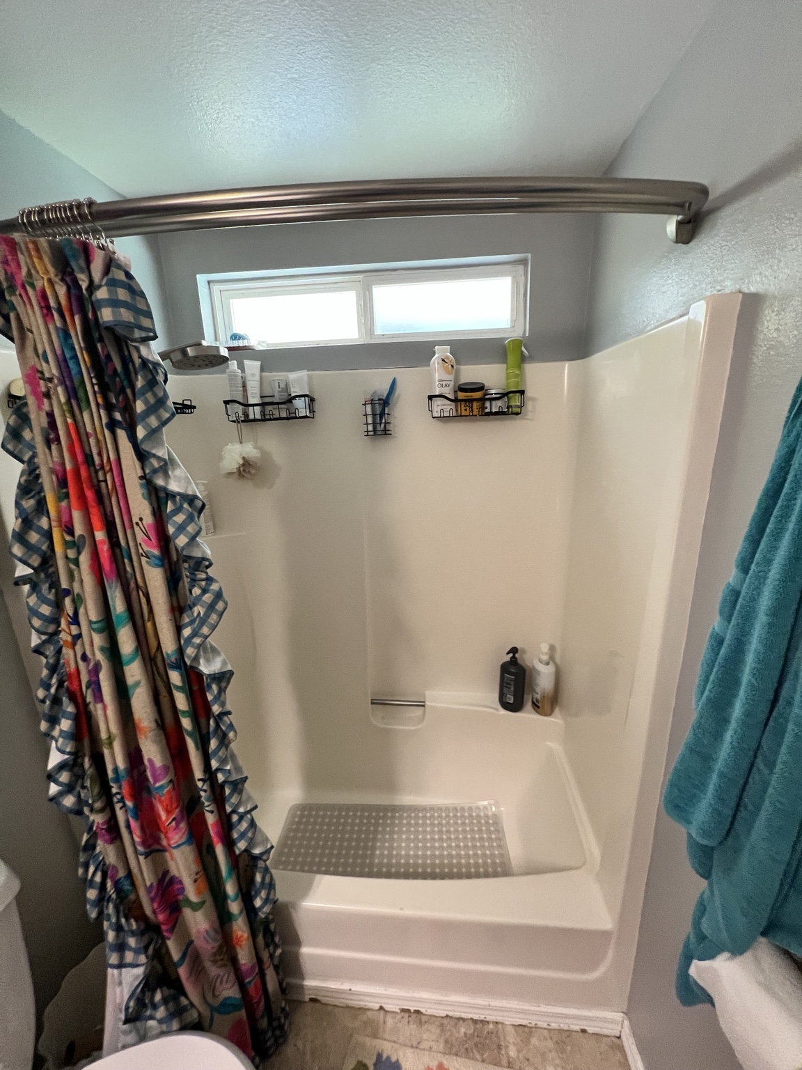 Original shower with a cream-colored surround, raised entry, and patterned shower curtain